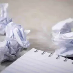 Zgniecione kartki papieru wokół notatnika, symbolizujące frustrację i potrzebę zasady YAGNI – nie dodawaj funkcjonalności, której nie potrzebujesz.