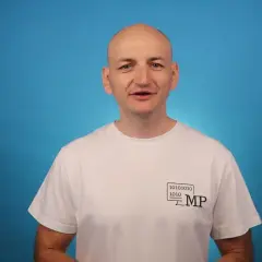 Mężczyzna w białej koszulce z logo MP i kodem binarnym opowiada o zaletach Blazor Server.