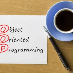 Kawa i długopis obok kartki z napisem "Object Oriented Programming". Rozważanie o **kompozycji vs dziedziczeniu** w OOP.