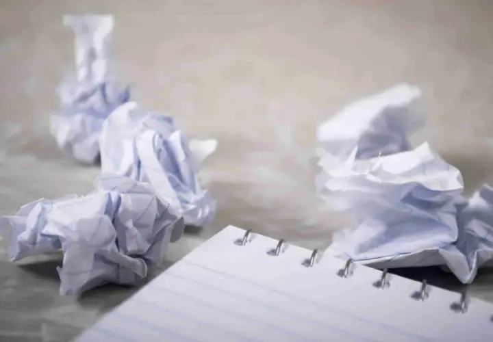 Zgniecione kartki papieru wokół notatnika, symbolizujące frustrację i potrzebę zasady YAGNI – nie dodawaj funkcjonalności, której nie potrzebujesz.