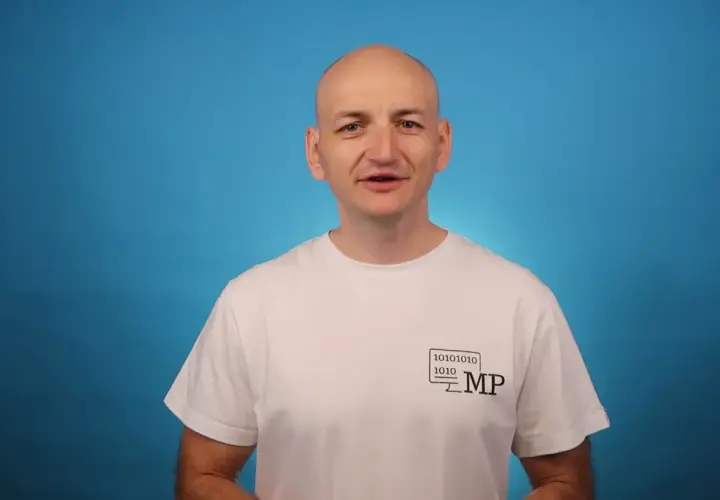 Mężczyzna w białej koszulce z logo MP i kodem binarnym opowiada o zaletach Blazor Server.
