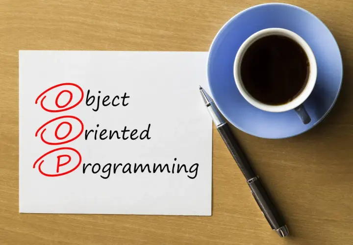 Kawa i długopis obok kartki z napisem "Object Oriented Programming". Rozważanie o **kompozycji vs dziedziczeniu** w OOP.