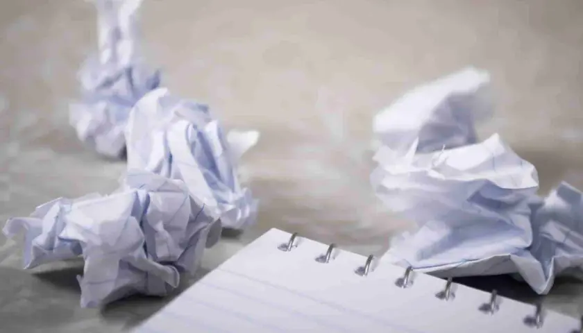 Zgniecione kartki papieru wokół notatnika, symbolizujące frustrację i potrzebę zasady YAGNI – nie dodawaj funkcjonalności, której nie potrzebujesz.