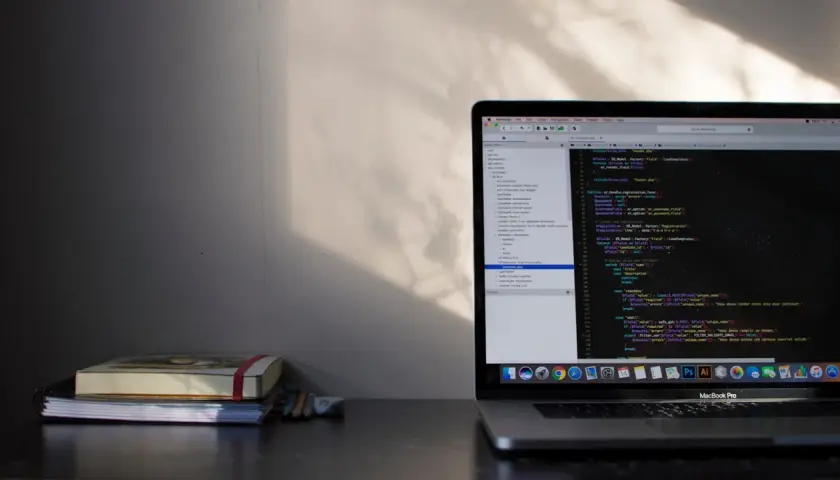 Na biurku leży stos książek, obok nich laptop z kodem PHP. Pętla `do while` jest widoczna na ekranie, gdzie programista pracuje nad projektem.