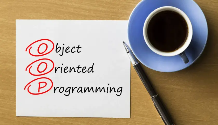 Kawa i długopis obok kartki z napisem "Object Oriented Programming". Rozważanie o **kompozycji vs dziedziczeniu** w OOP.