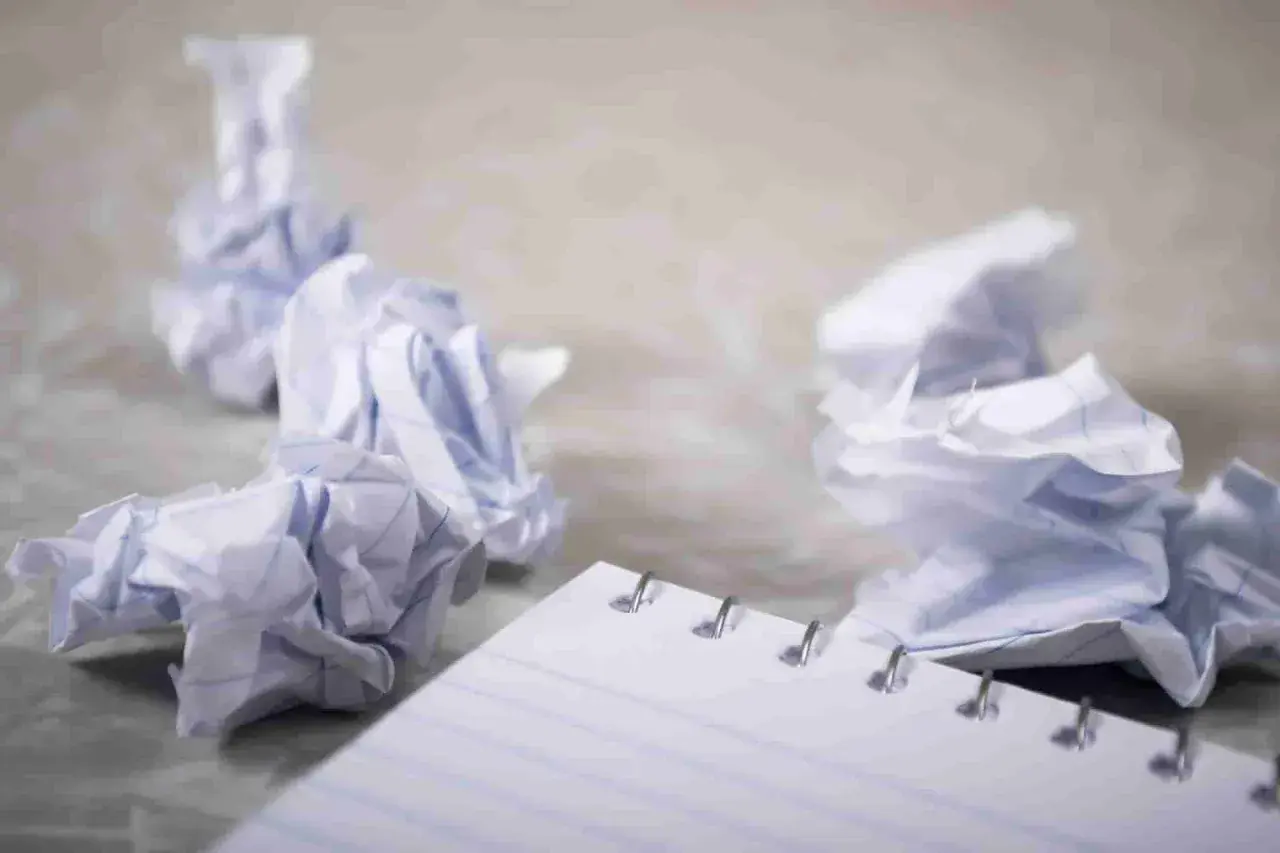 Zgniecione kartki papieru wokół notatnika, symbolizujące frustrację i potrzebę zasady YAGNI – nie dodawaj funkcjonalności, której nie potrzebujesz.