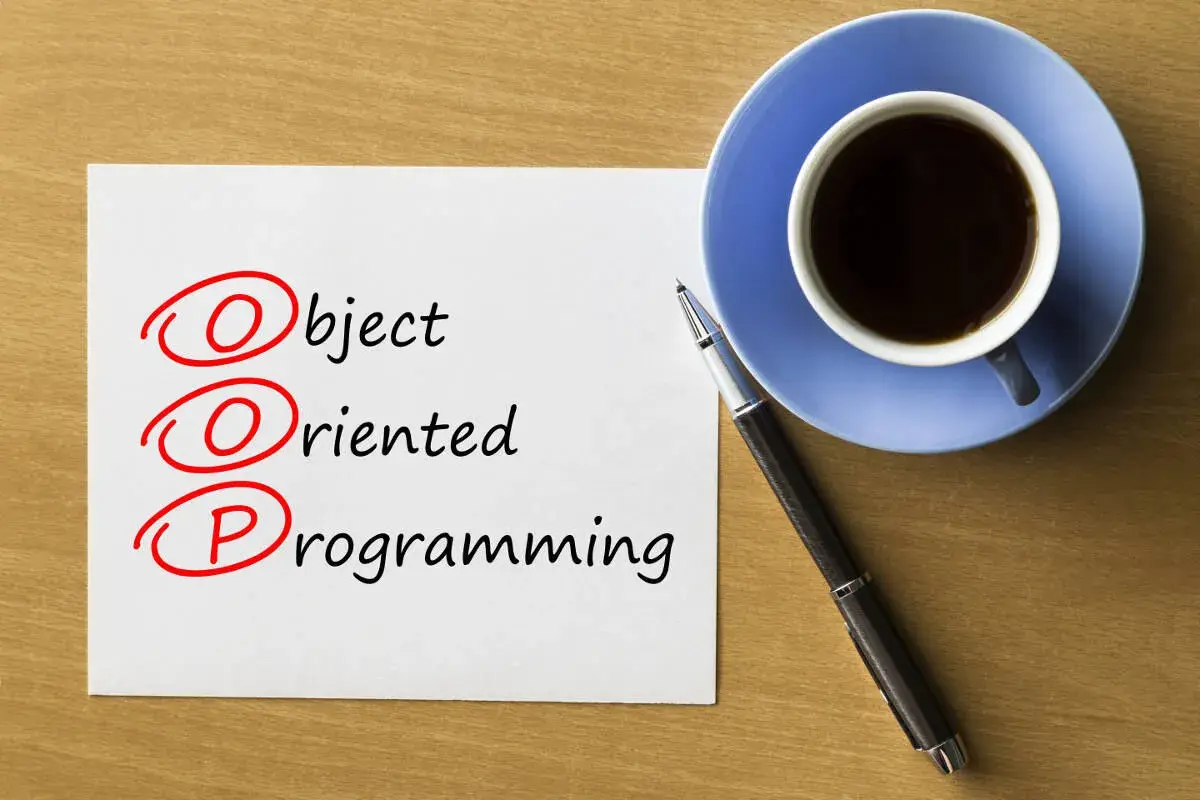 Kawa i długopis obok kartki z napisem "Object Oriented Programming". Rozważanie o **kompozycji vs dziedziczeniu** w OOP.